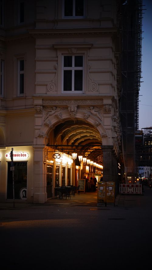 Free Illuminated archway in a European city at twilight, showcasing classic architecture and street cafes. Stock Photo