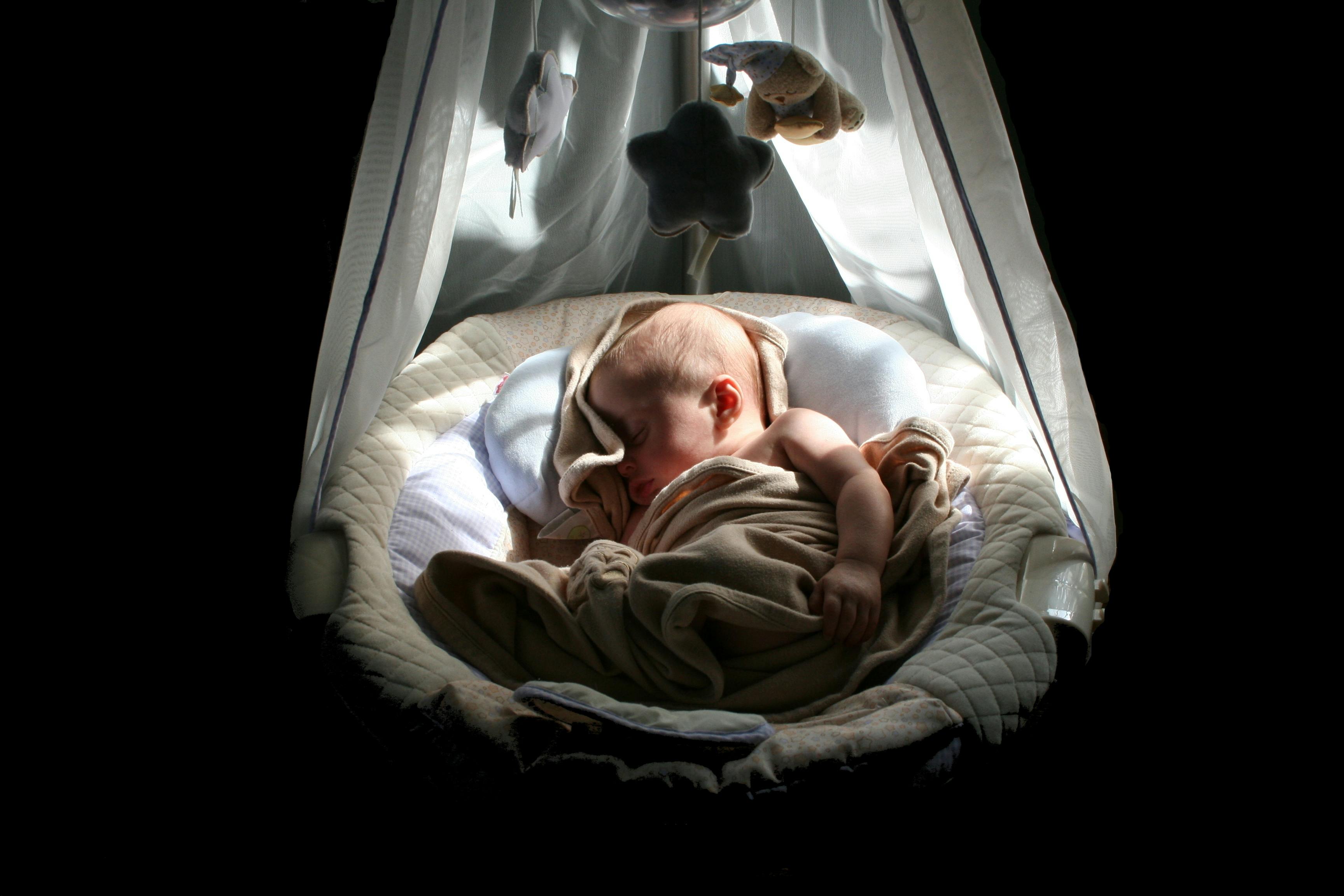 A calm baby sleeps soundly in a cozy, well-lit cradle under a mobile.