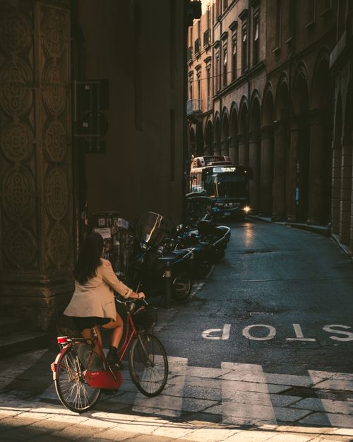 Free A cyclist rides down a historic street at sunset, casting dramatic shadows. Stock Photo