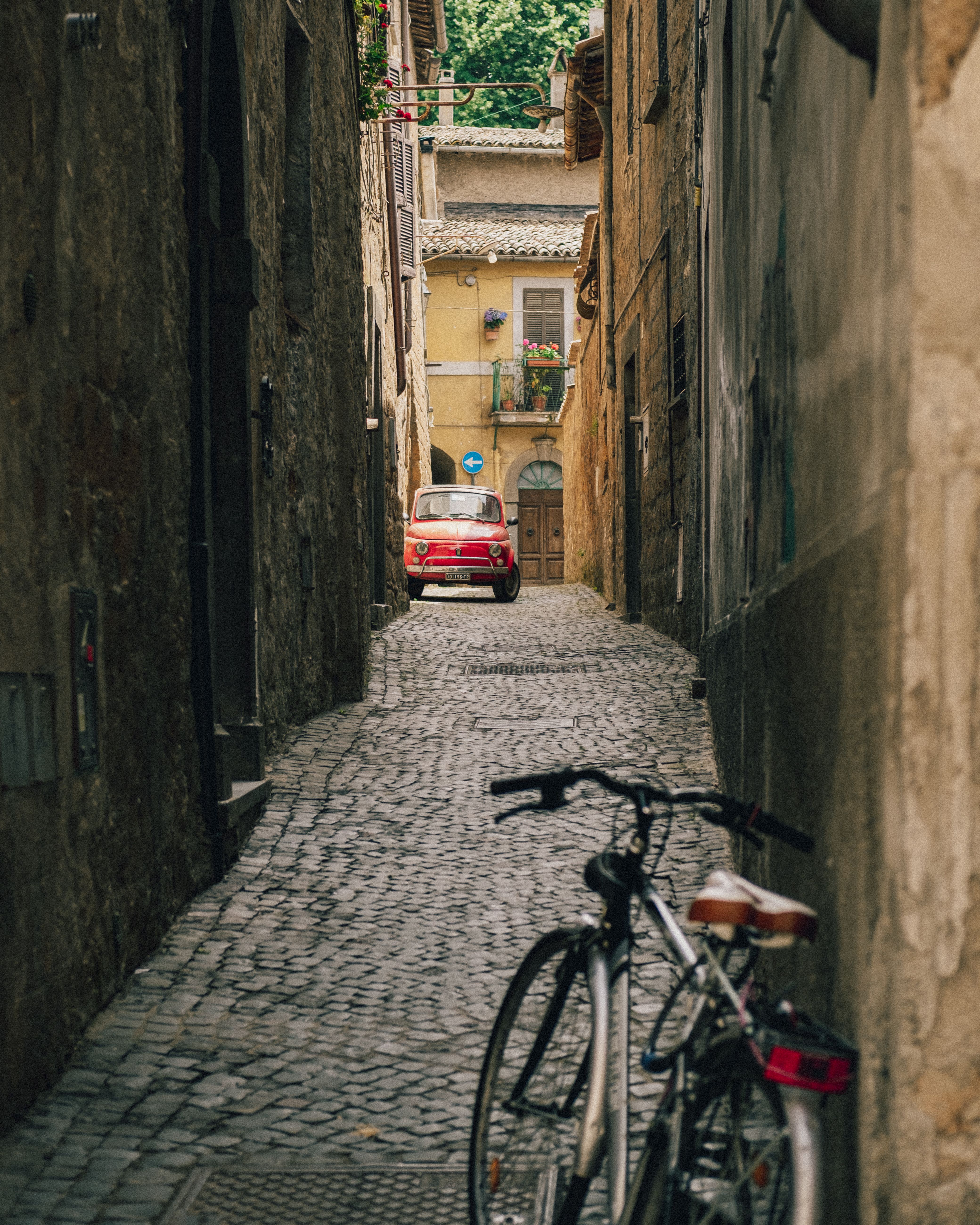A picturesque narrow alleyway in Italy with a classic red Fiat car and a bicycle.