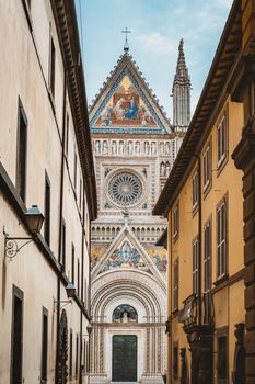 Captivating view of the intricate façade of Orvieto Cathedral in Italy, framed by surrounding buildings on a clear day.