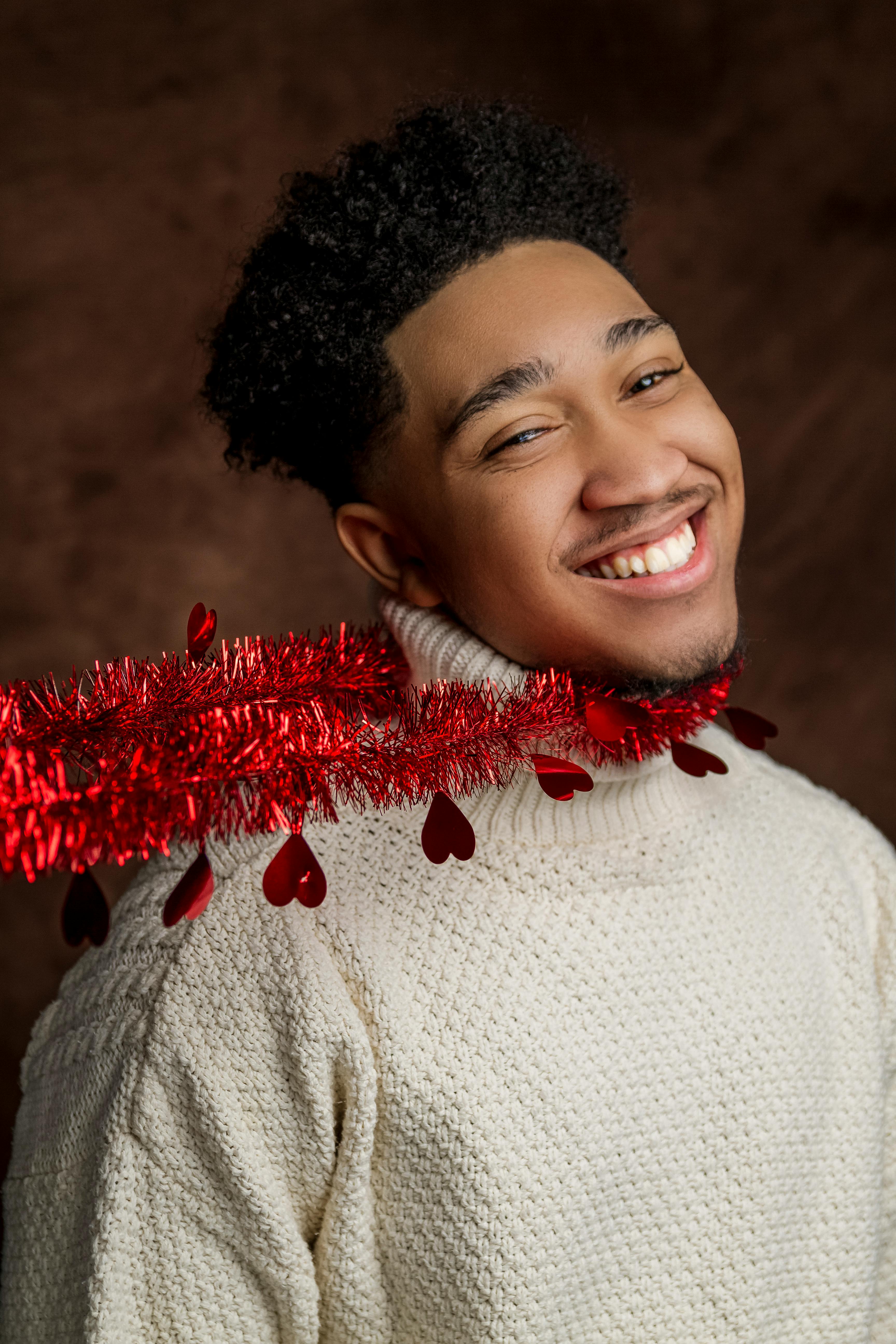 一位身穿白色针织衫、脖子上挂着红色节日花环的男子，在工作室里微笑着拍摄了肖像