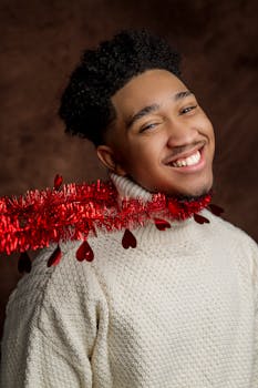 一位身穿白色针织衫、脖子上挂着红色节日花环的男子，在工作室里微笑着拍摄了肖像