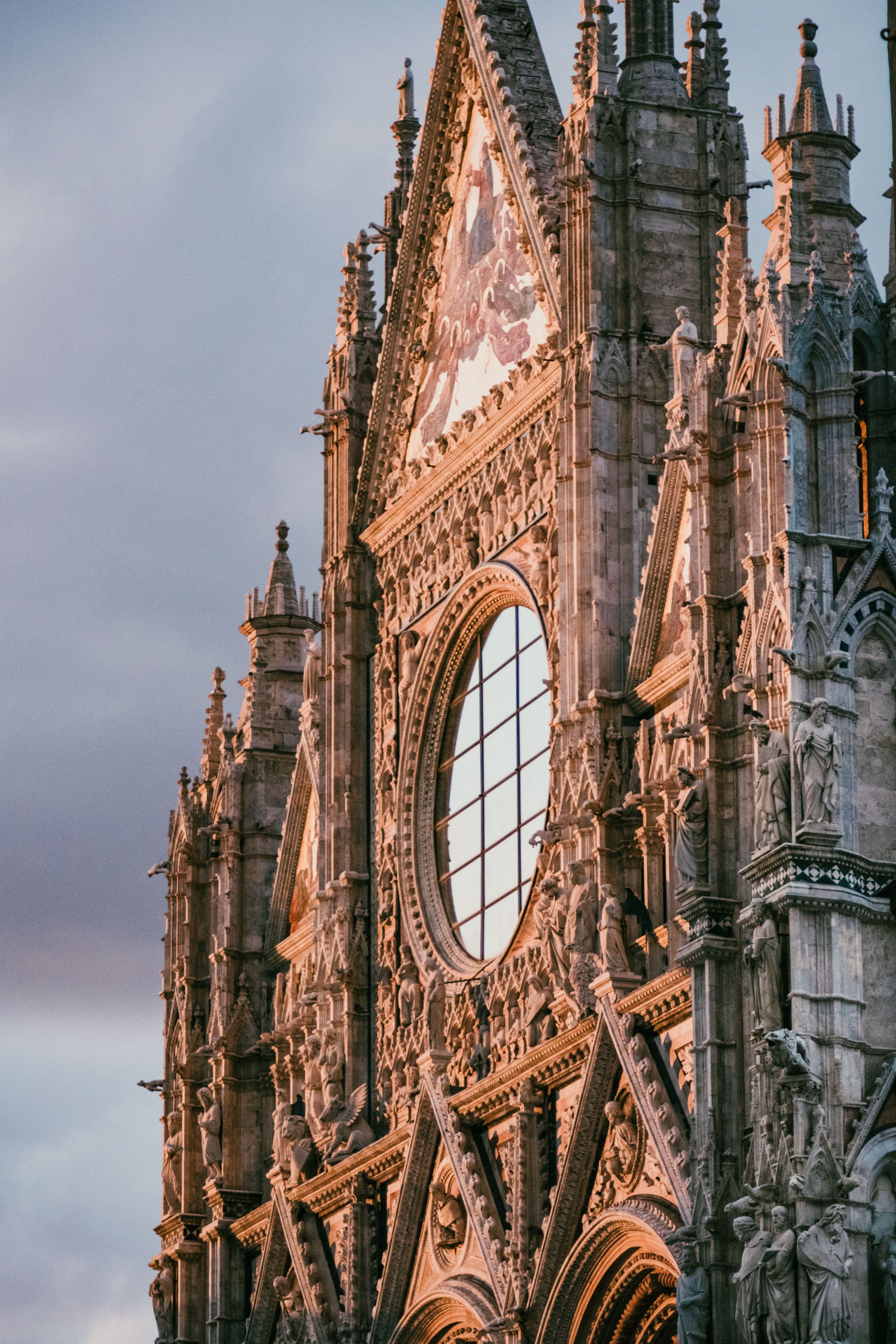 Detailed view of the ornate Gothic facade of the Duomo di Siena at sunset, capturing its intricate design.
