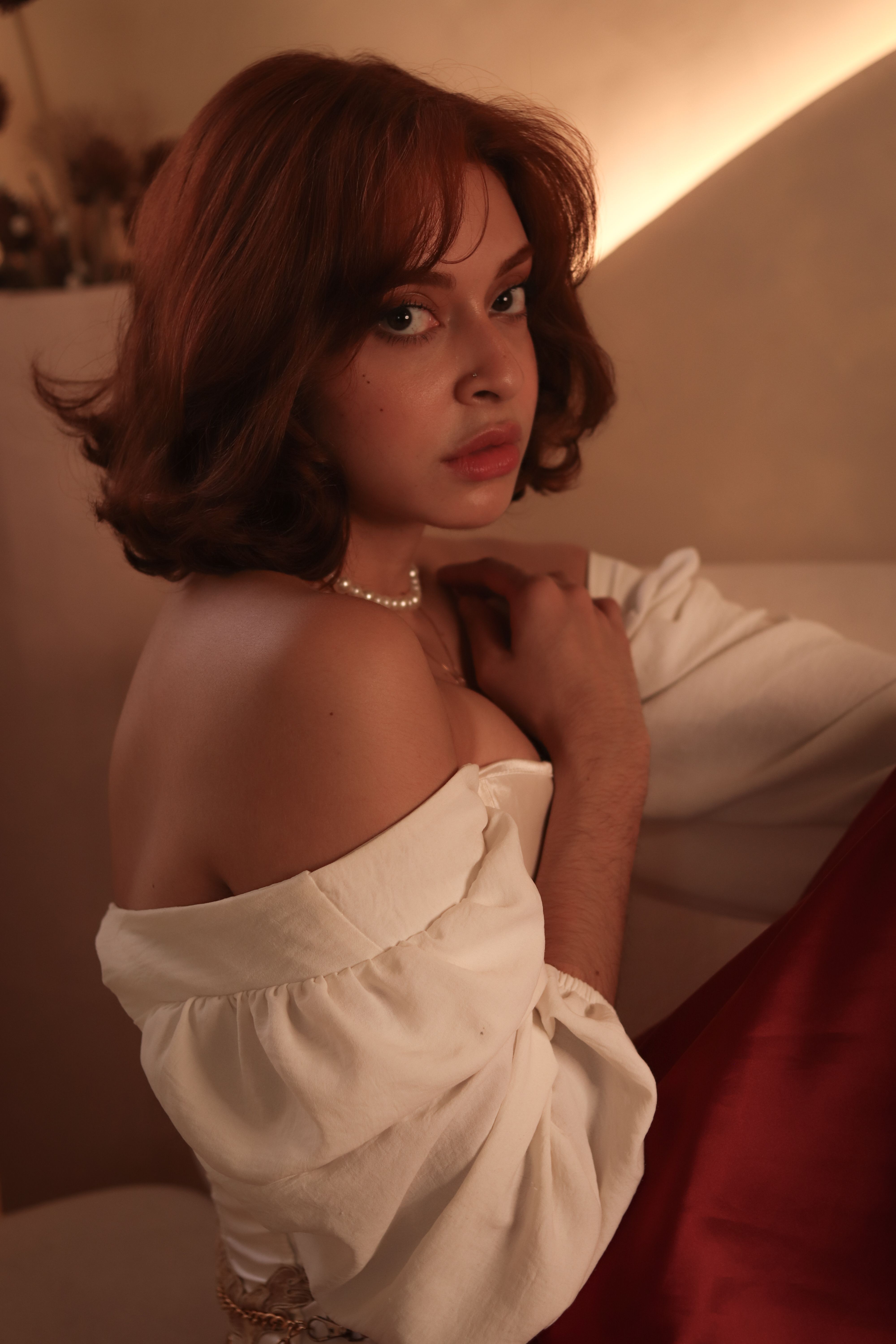 Intimate portrait of a young woman with auburn hair in warm lighting indoors.