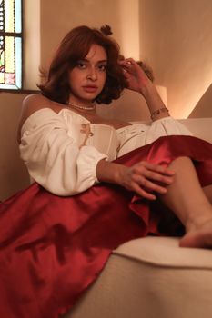 A woman in elegant attire relaxing on a sofa with soft lighting indoors.