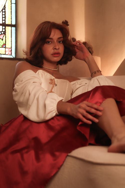 Free A young woman in elegant attire relaxes on a couch in a softly lit room. Stock Photo