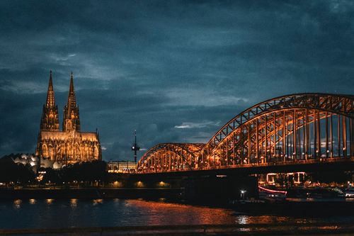 Cologne Cathedral and Hohenzollern Bridge beautifully illuminated at night reflecting over the Rhine River.