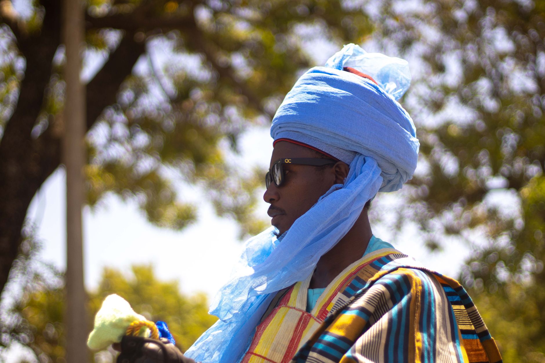 A man in traditional Nigerian attire with a colorful turban standing outdoors during the day.
