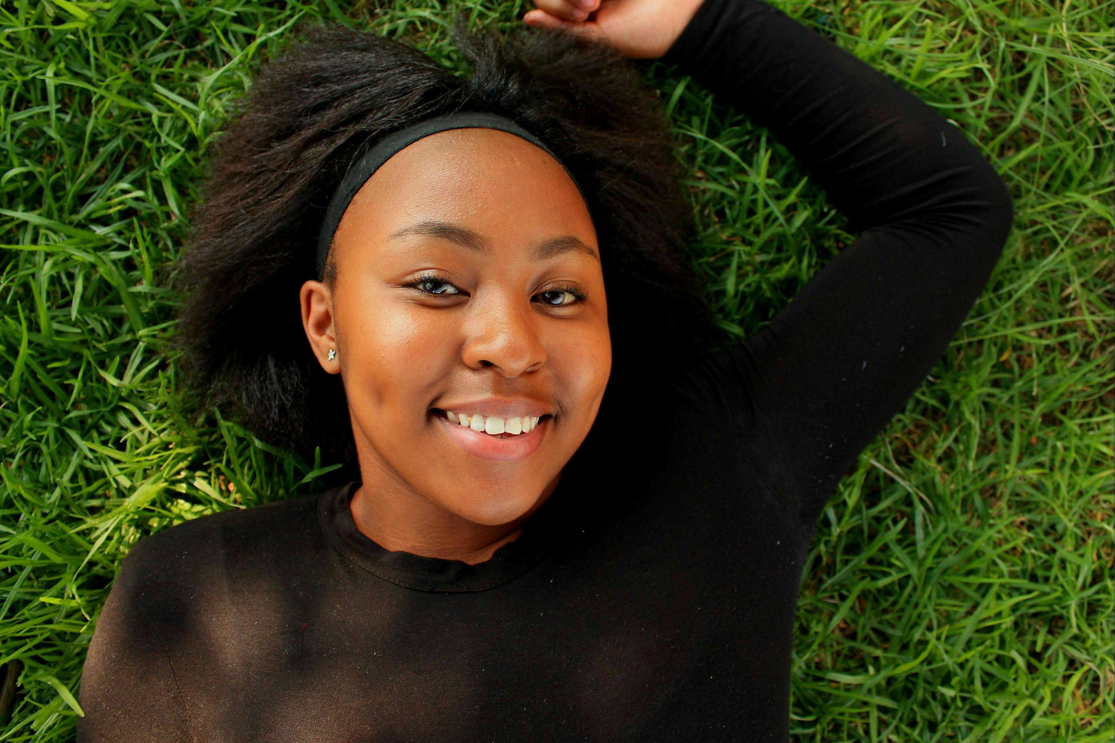 Happy young woman smiling while lying on green grass in a park.