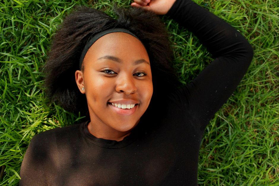 Happy young woman smiling while lying on green grass in a park.