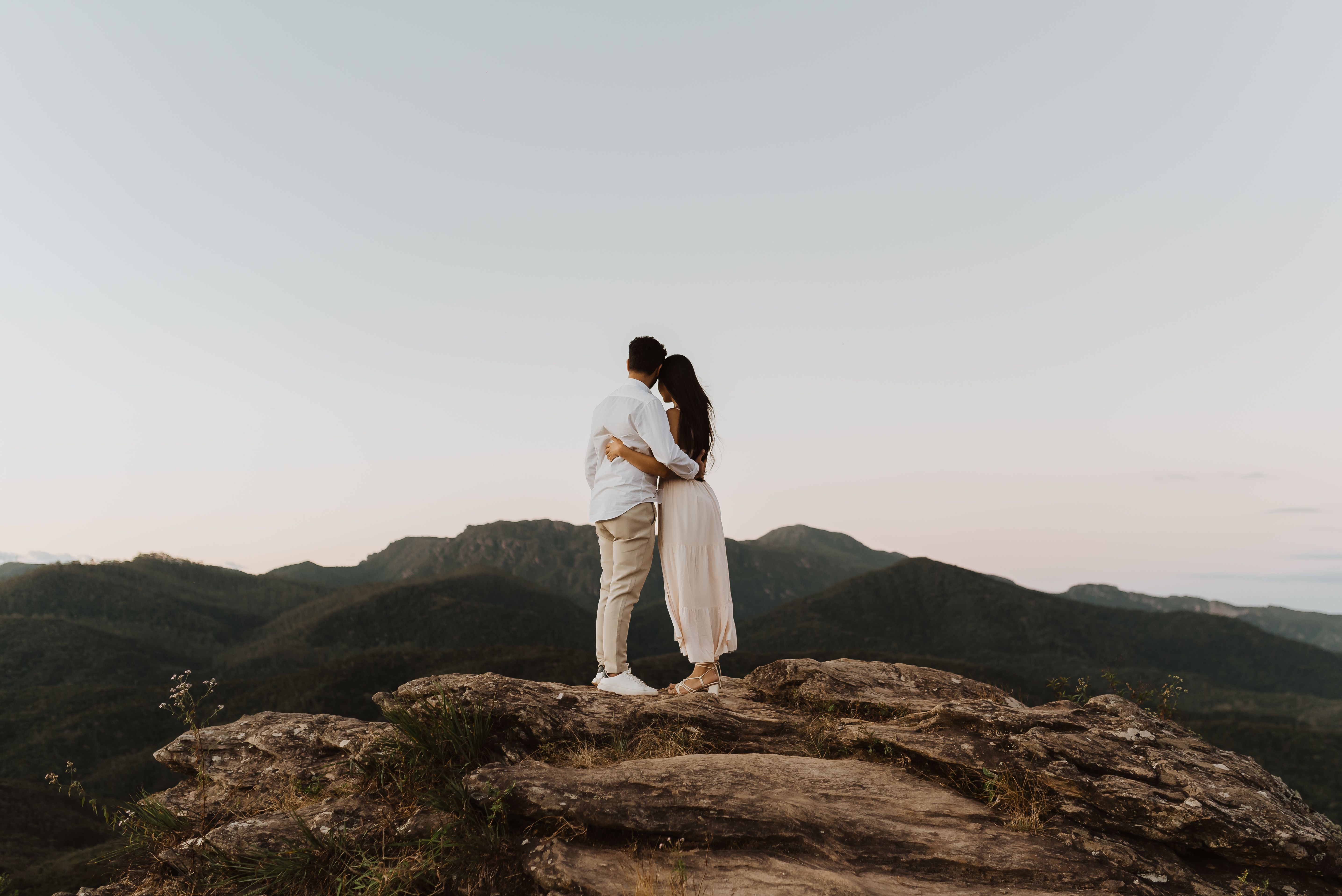 Romantic couple embracing on a mountain top during sunset, surrounded by nature.