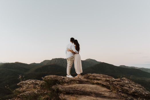 Romantic couple embracing on a mountain top during sunset, surrounded by nature.