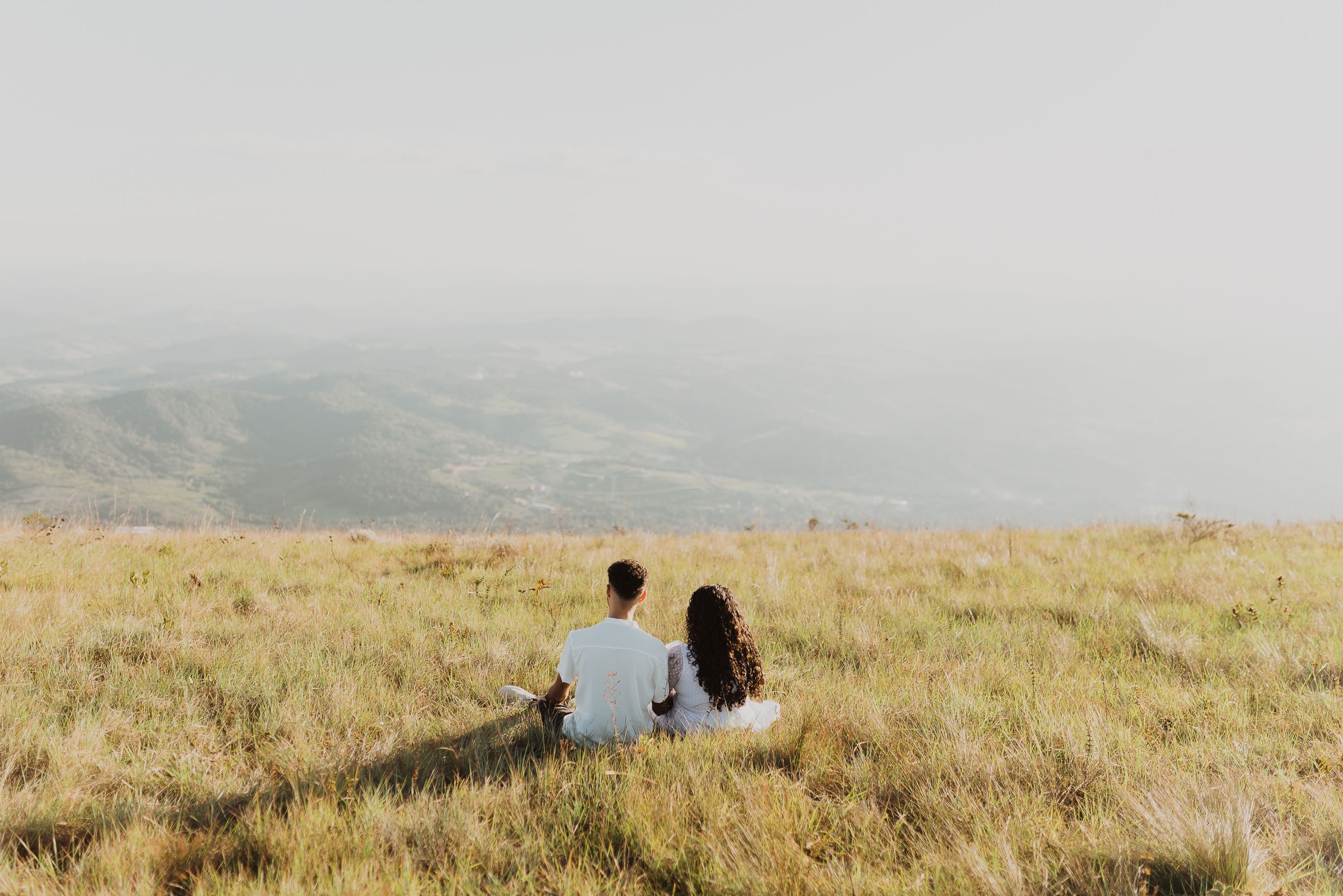 A couple sitting on a grassy hill, enjoying a distant mountain view.