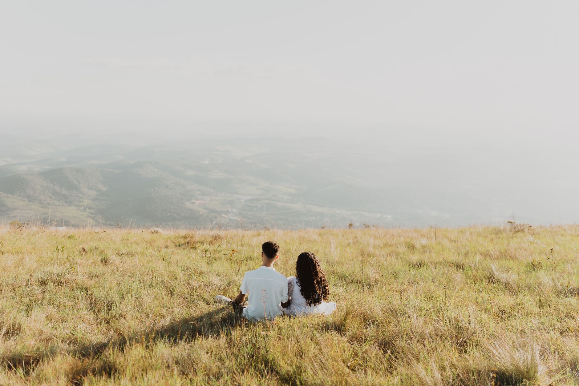 A couple sitting on a grassy hill, enjoying a distant mountain view.