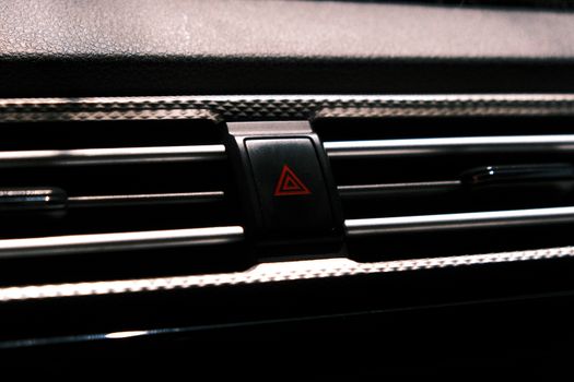 Close-up image of a car hazard light button on a dark dashboard.