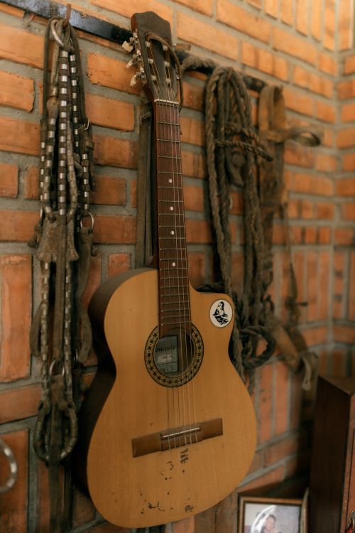 Free Vintage acoustic guitar hanging on a brick wall, adding rustic charm to the indoor decor. Stock Photo