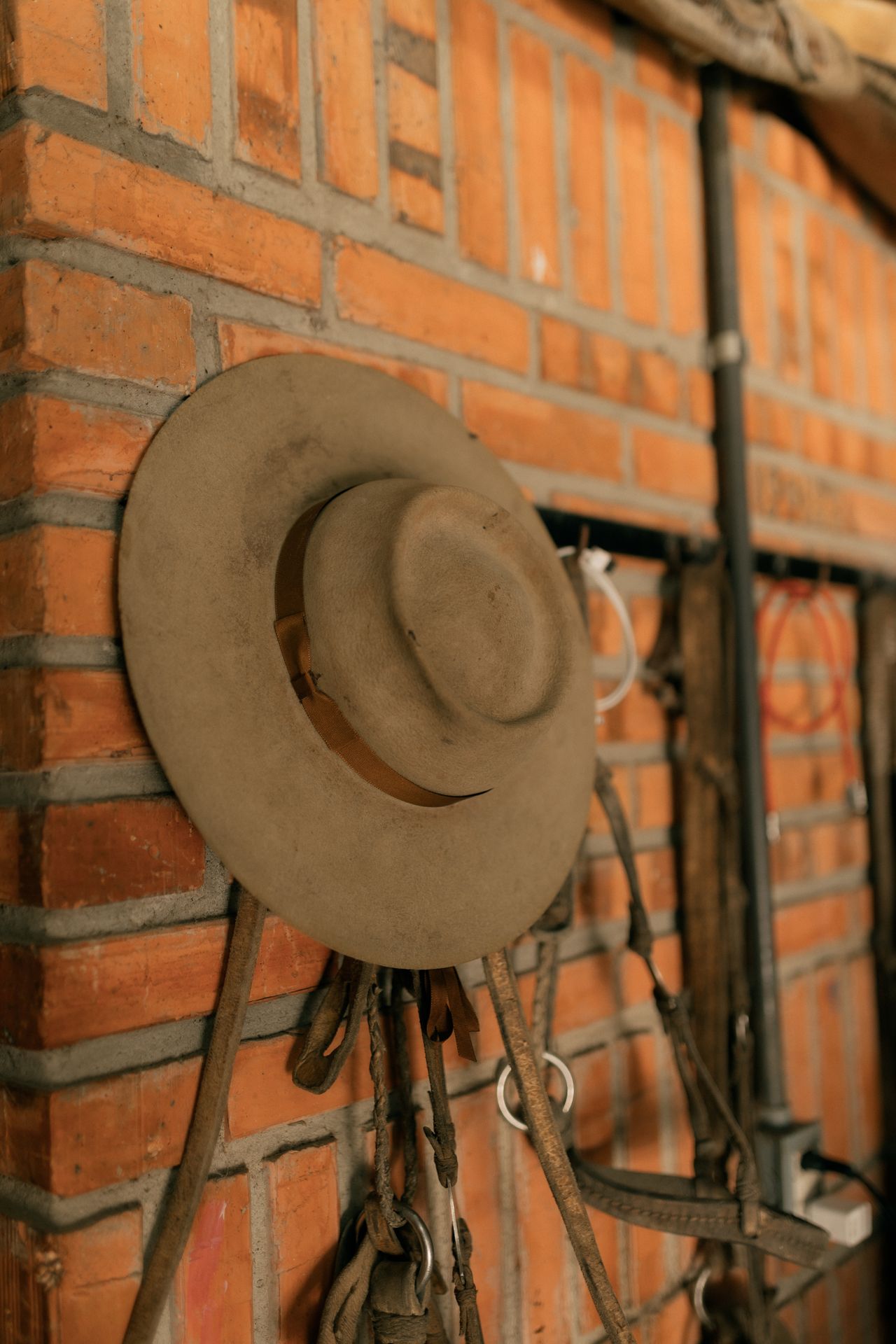 Vintage cowboy hat hanging on a brick wall beside leather tack