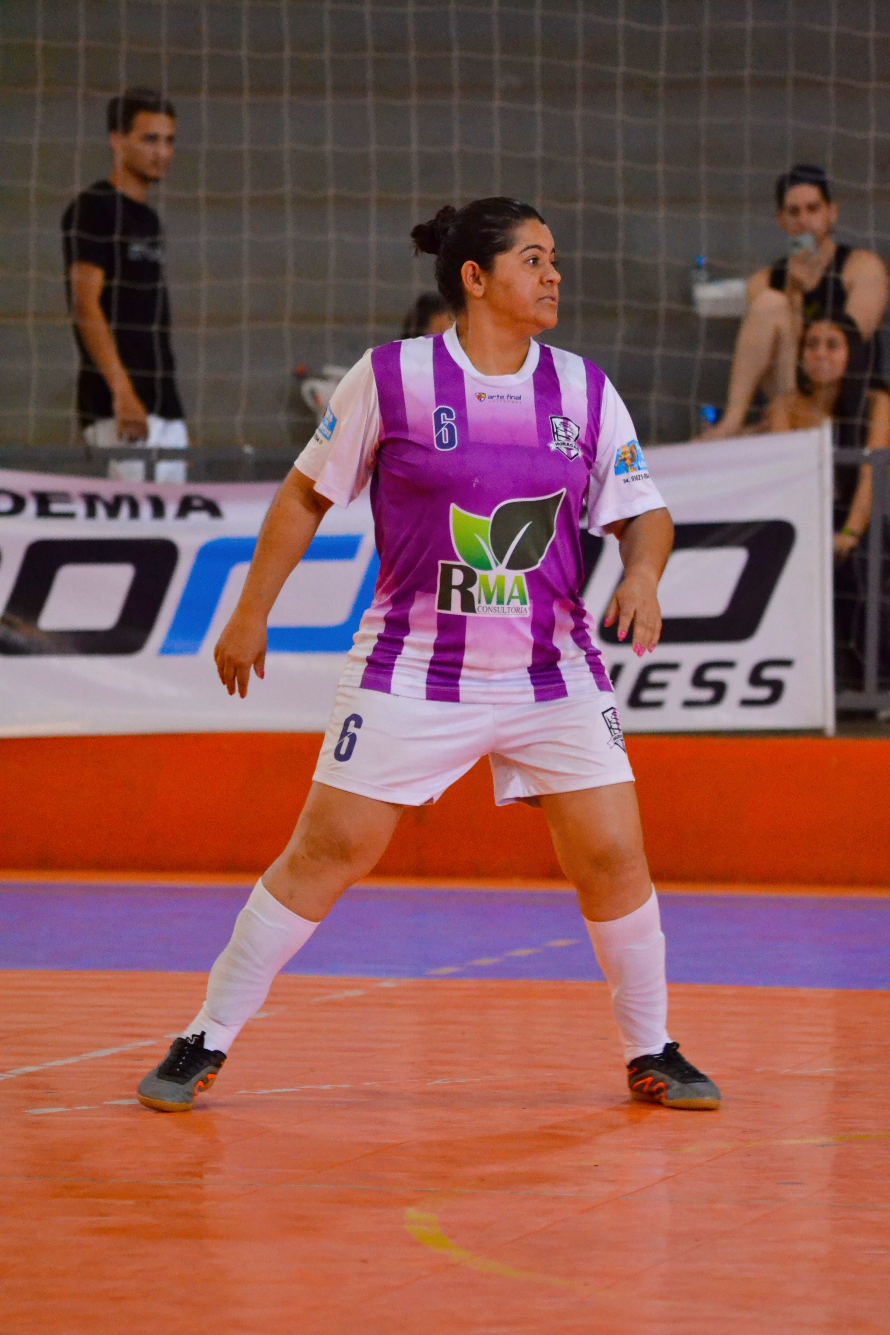 Female indoor soccer player in purple and white uniform at the ready during a match.