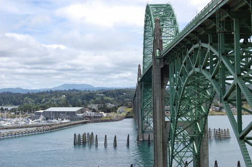Free Green steel arch bridge spanning over a serene bay with marina and forested hills in the background. Stock Photo