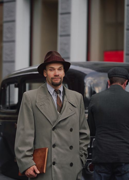 Free A man in vintage attire stands beside a classic car in Riga, exuding an old-world charm. Stock Photo
