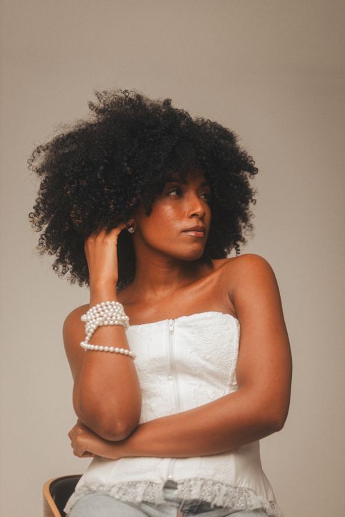 Free Portrait of a woman with curly hair and pearl bracelets, wearing a white top. Stock Photo