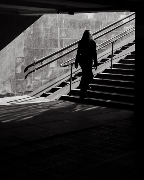 Free A woman in silhouette walks up stairs in a shadowy urban setting, black and white. Stock Photo
