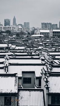 Aerial view of snow-covered traditional rooftops contrasting with modern city skyline.