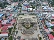 Aerial shot of a cityscape featuring a central building with circular architecture, surrounded by colorful rooftops.