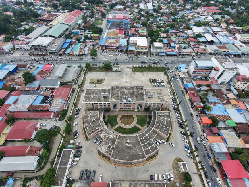 Aerial shot of a cityscape featuring a central building with circular architecture, surrounded by colorful rooftops.