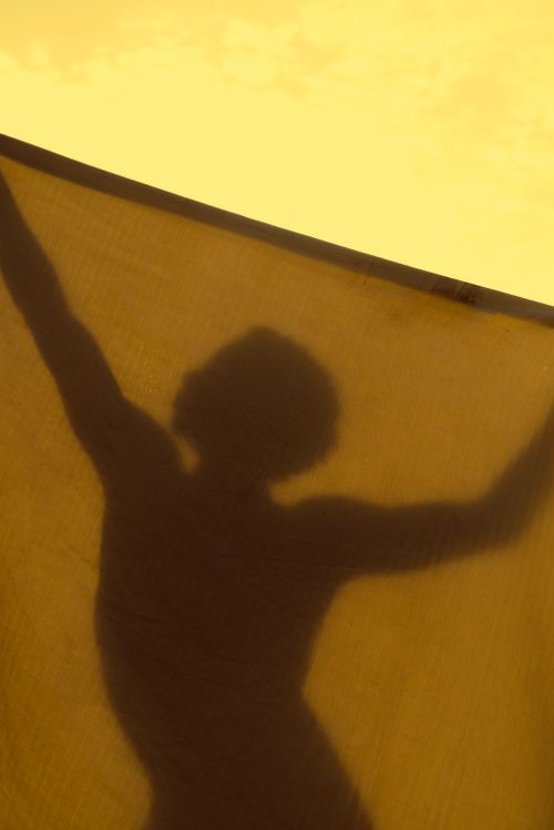 Free Artistic silhouette of a person behind a sheer fabric with golden light creating a dramatic shadow effect. Stock Photo