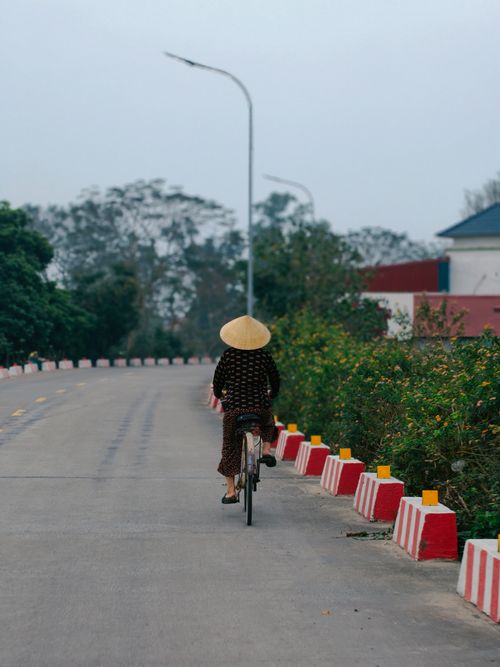 Free A lone woman in traditional rice hat cycling down a peaceful rural road. Stock Photo