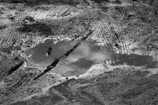Black and white photo of a puddle reflecting the sky on a dirt road.