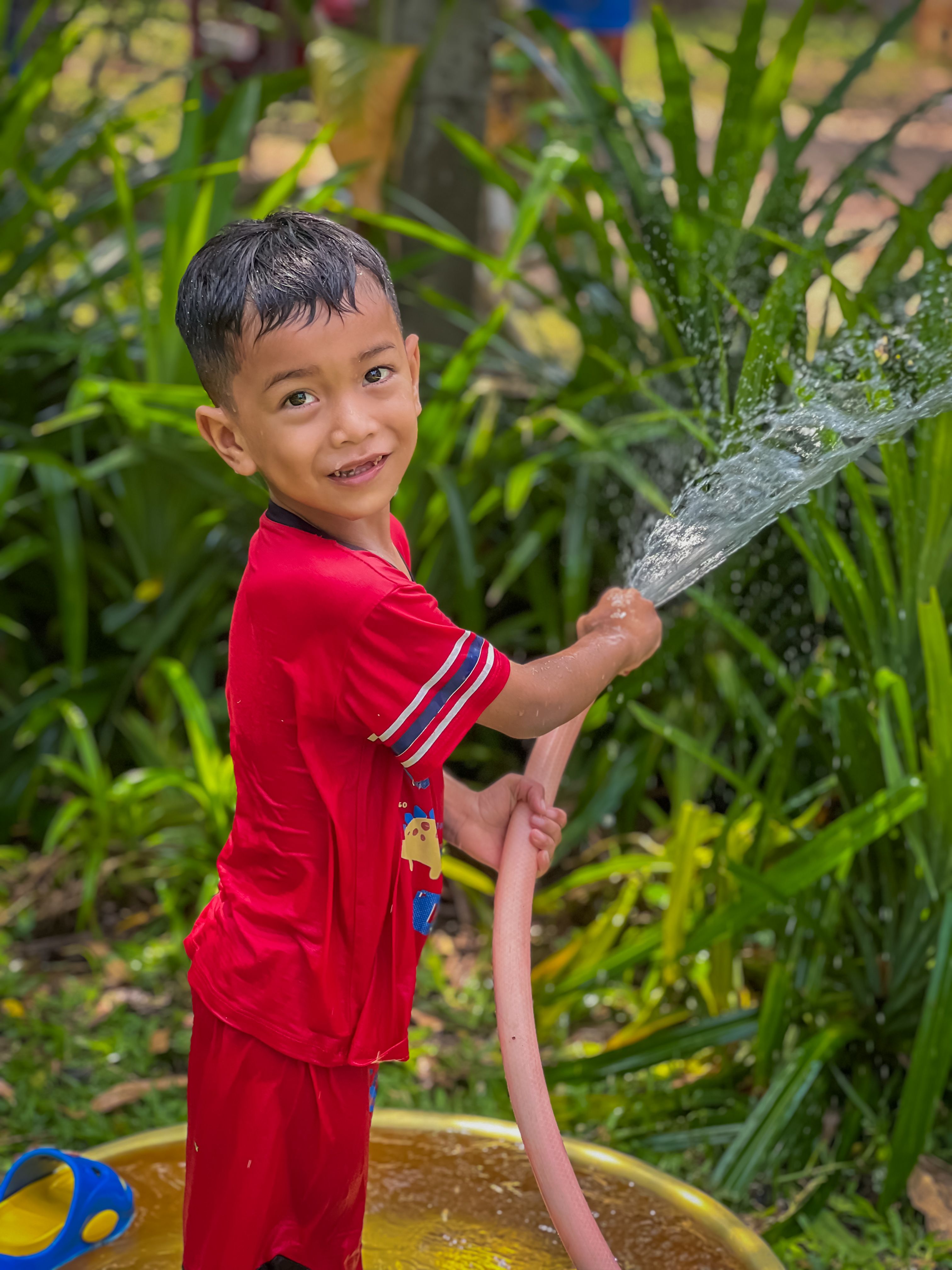A joyful child in red enjoying outdoor water play with garden hose.