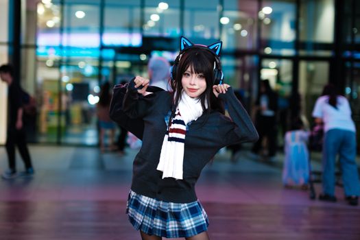 Cosplayer with cat ear headphones poses playfully outside at night, creating a vibrant urban scene.