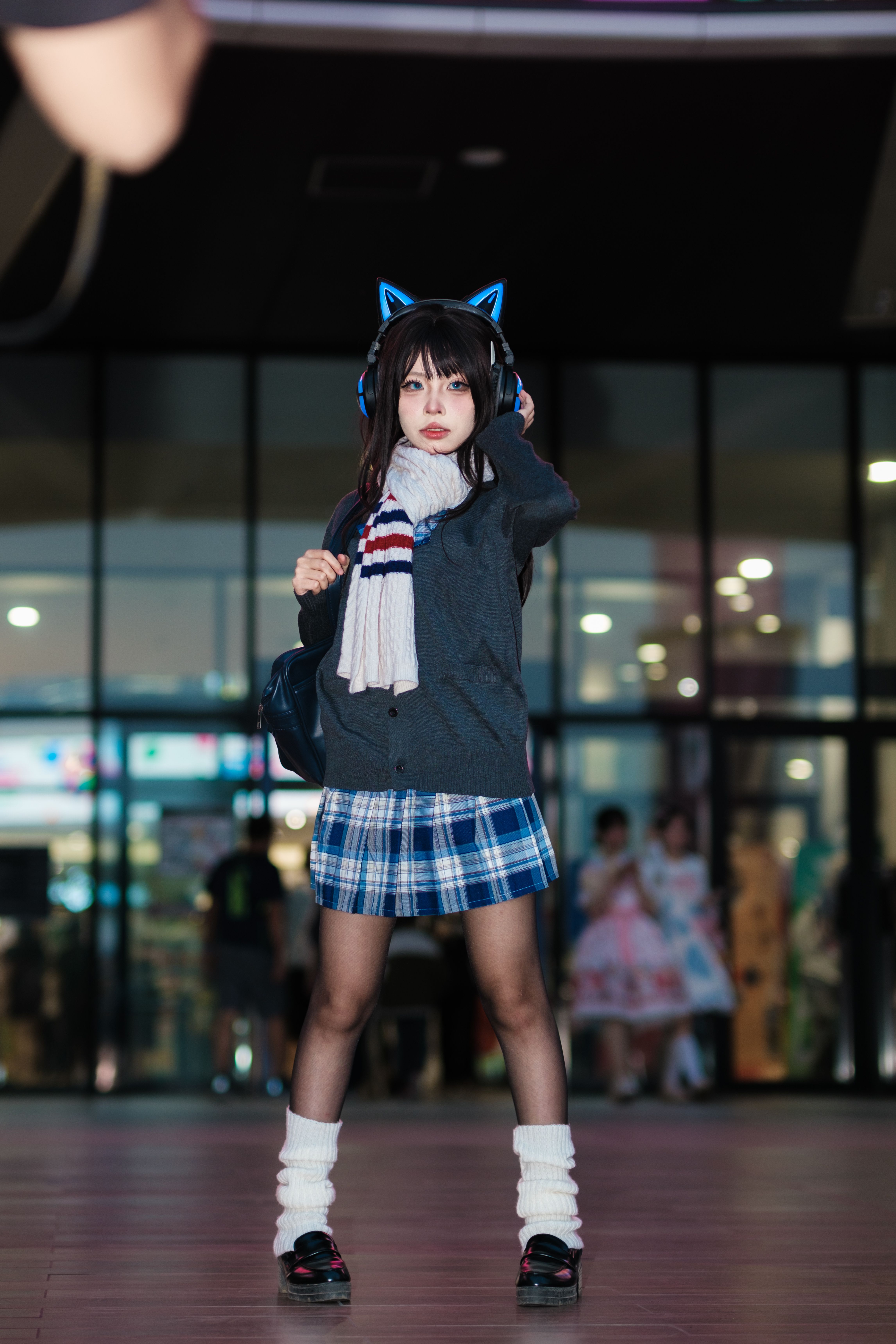 A teenager in trendy attire and cat ear headphones poses confidently indoors.