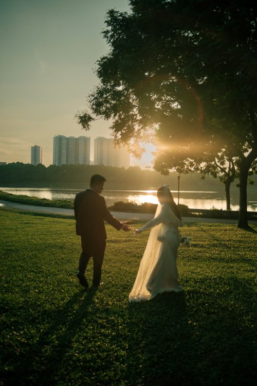 Free Silhouette of a bride and groom holding hands during a sunset by the water, creating a romantic atmosphere. Stock Photo