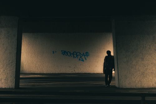 Free Silhouetted person walking in a dimly lit urban tunnel with graffiti, creating a mysterious atmosphere. Stock Photo