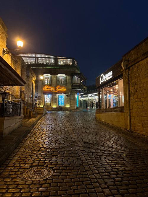 Free Illuminated cobblestone street with shops at night, creating a cozy atmosphere. Stock Photo
