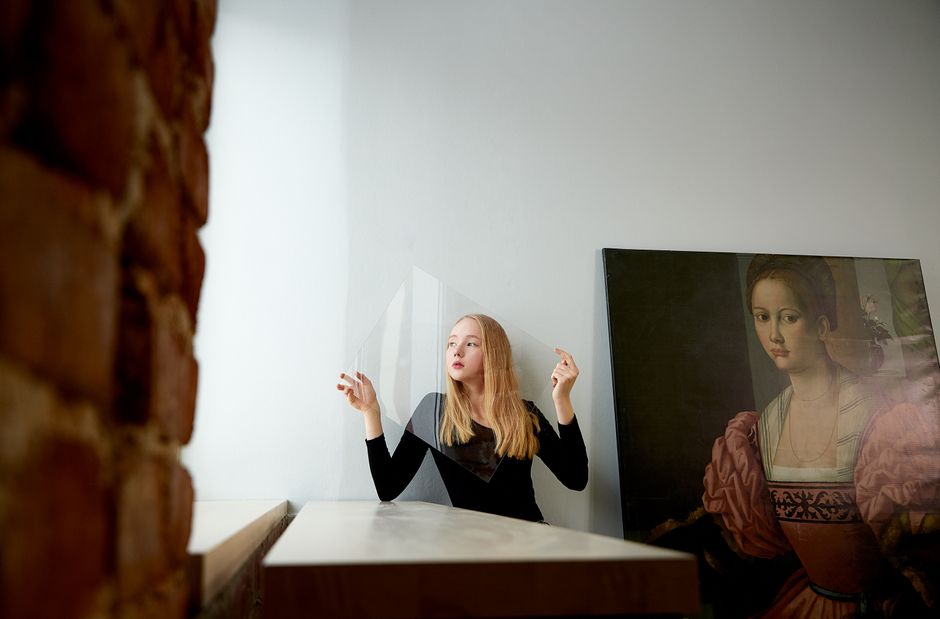 Elegant portrait of a woman posing indoors next to a classic artwork in a studio setting.