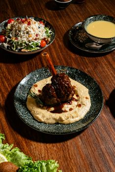 A gourmet lamb shank served on creamy hummus with sides, perfect for culinary inspiration.