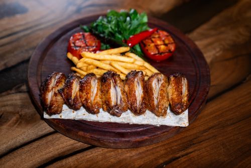 Free Mouth-watering grilled chicken wings with vegetables, fries, and greens on a wooden platter. Stock Photo