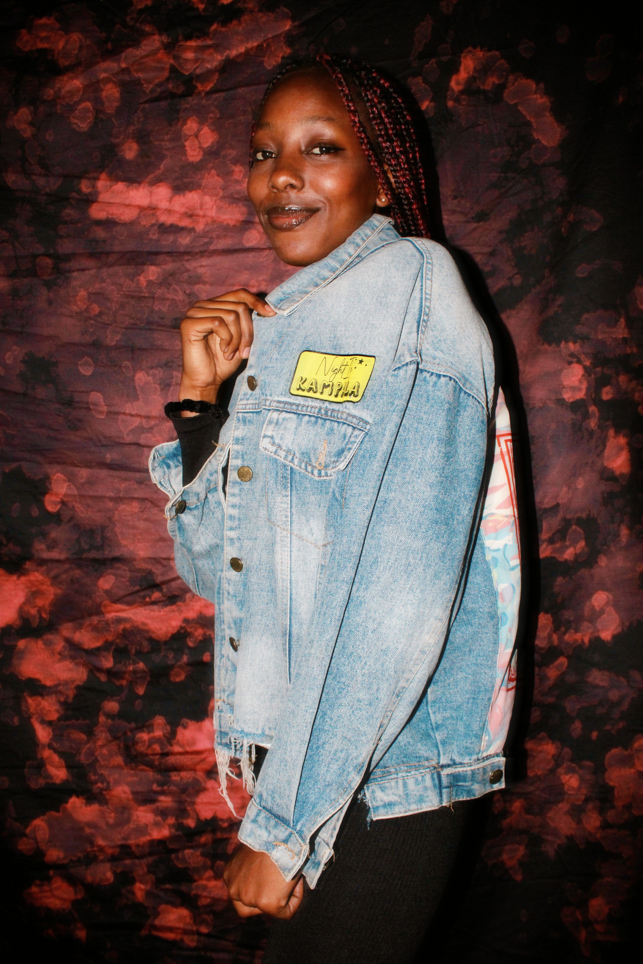 Woman posing confidently in denim jacket with artistic background.