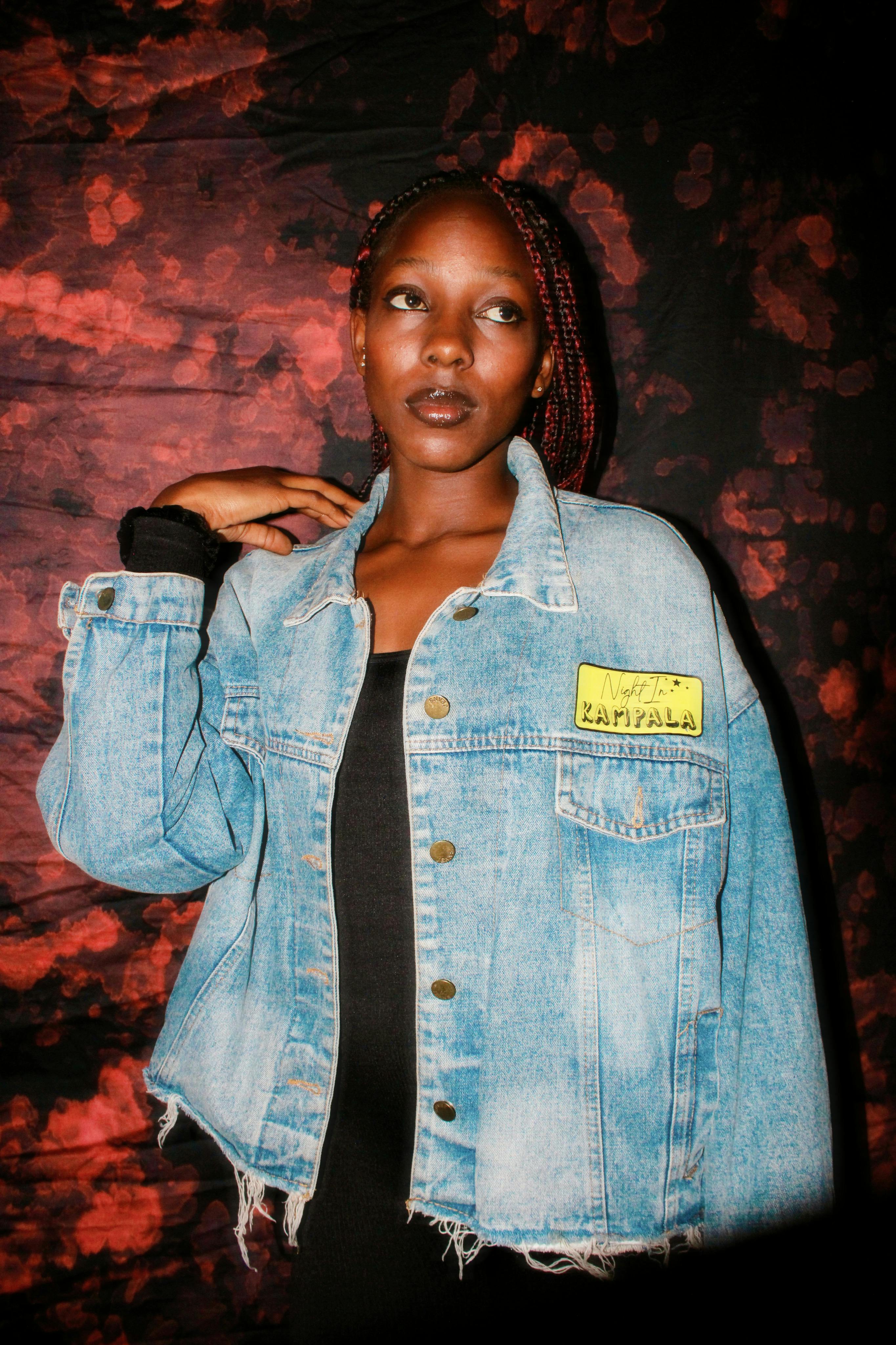 Fashionable woman wearing a denim jacket posing against a vibrant artistic background.