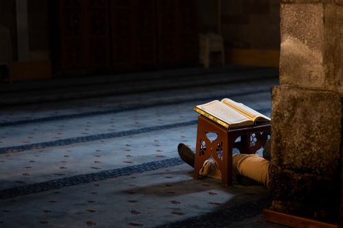 Free A person praying quietly in a dimly lit mosque with an open Quran, highlighting peace and devotion. Stock Photo