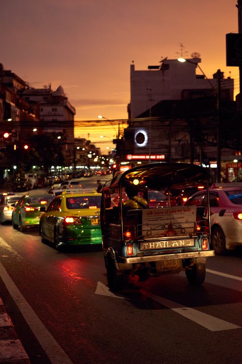Free Vibrant Bangkok street scene featuring a tuk tuk amidst city traffic during sunset. Stock Photo