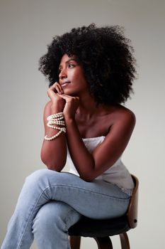 Portrait of an elegant woman with natural curly hair and pearl bracelets, seated indoors.