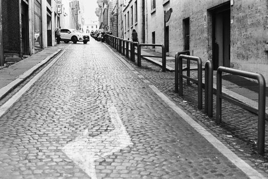 Black and white photo of a cobblestone street in Rome with a lone pedestrian.