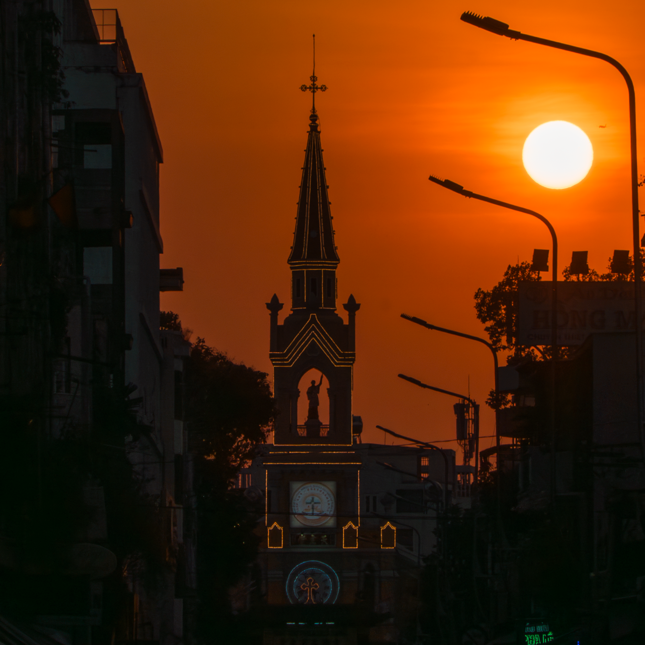 Silhouette of a church tower against a vivid sunset sky, street lamps in view.