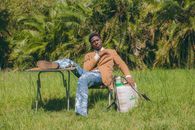 Man in casual attire relaxes with a sprayer outdoors amidst lush greenery in Accra, Ghana.